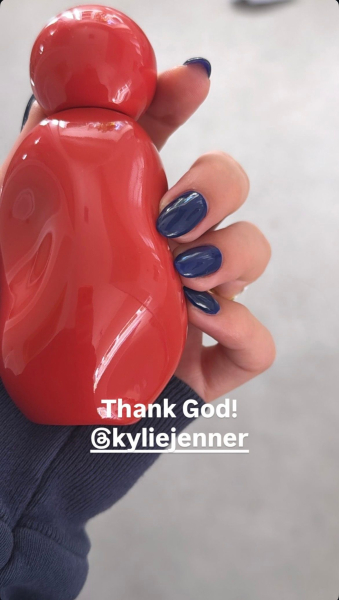 Hailey Bieber holds a perfume bottle with navy blue nails.